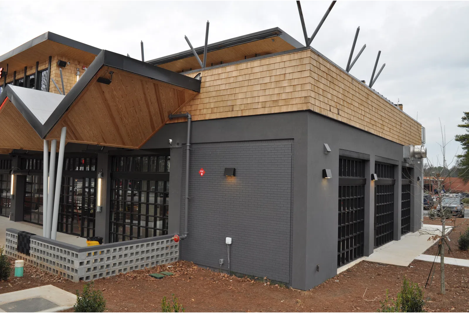 Modern commercial building with gray brick walls, wooden accents, large windows, and geometric roof design