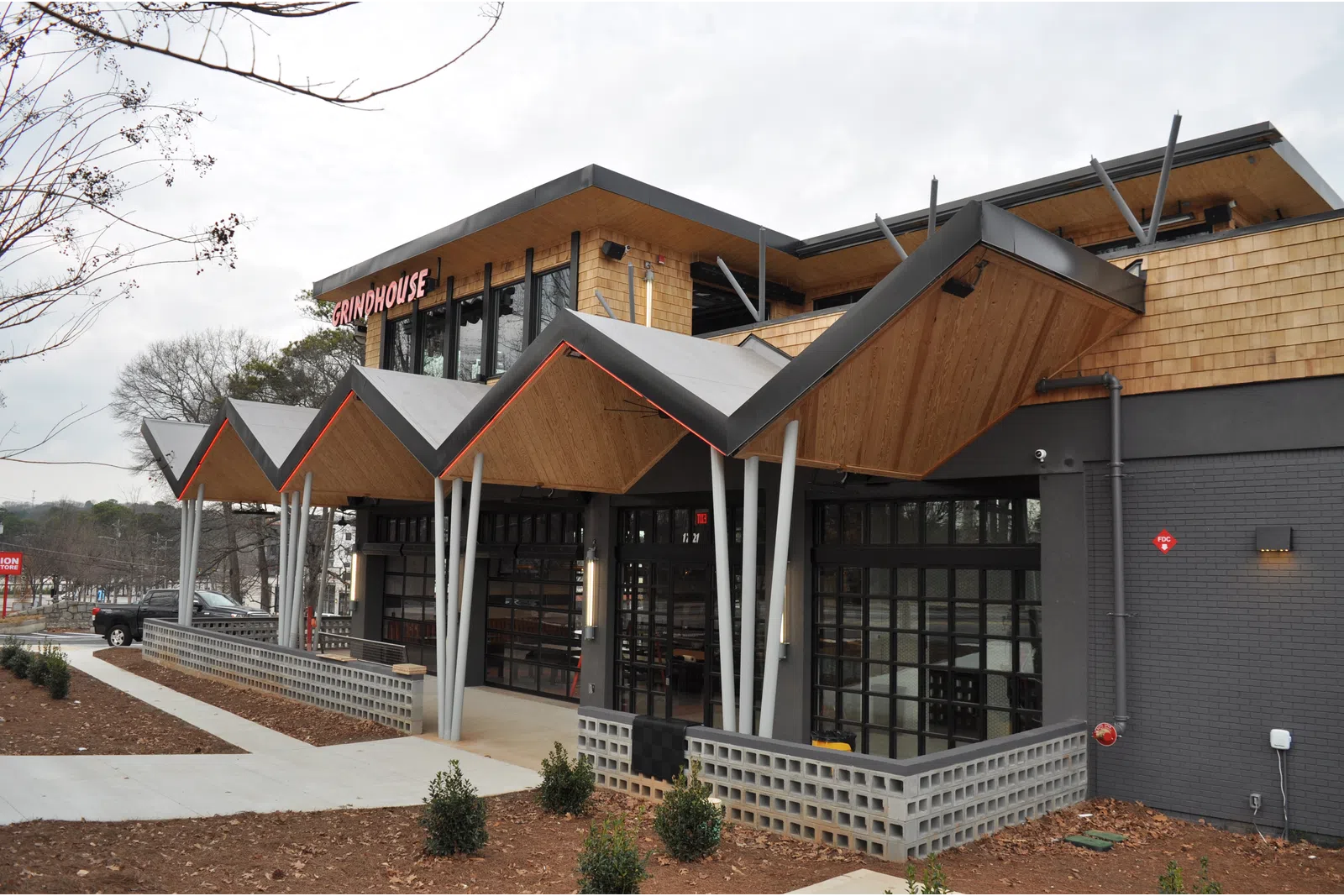 Modern restaurant exterior with geometric roof design, wooden accents, large windows, and landscaped surroundings.