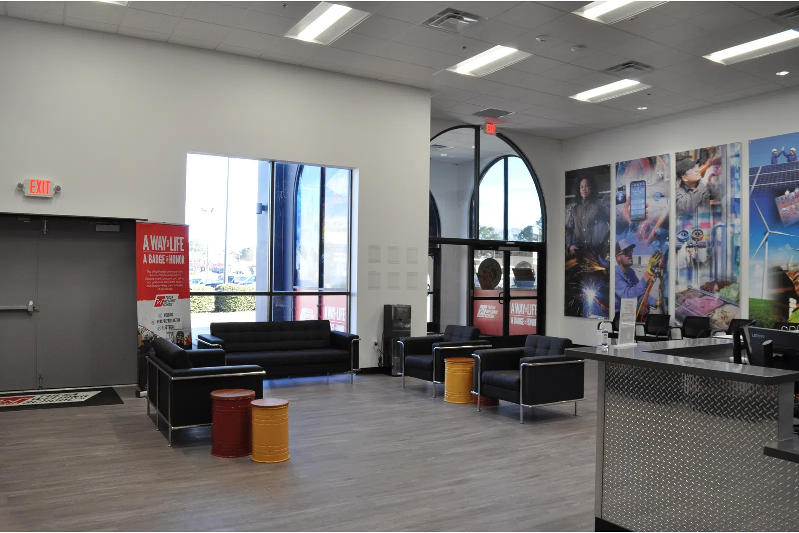 Modern lobby area with black sofas, colorful barrel stools, large windows, and vibrant wall murals advertising a trade organization.