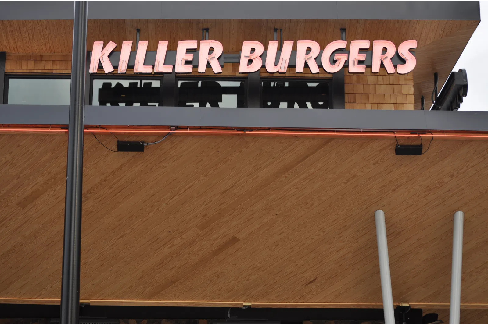 KILLER BURGERS restaurant sign with pink neon letters mounted on a wooden exterior wall.