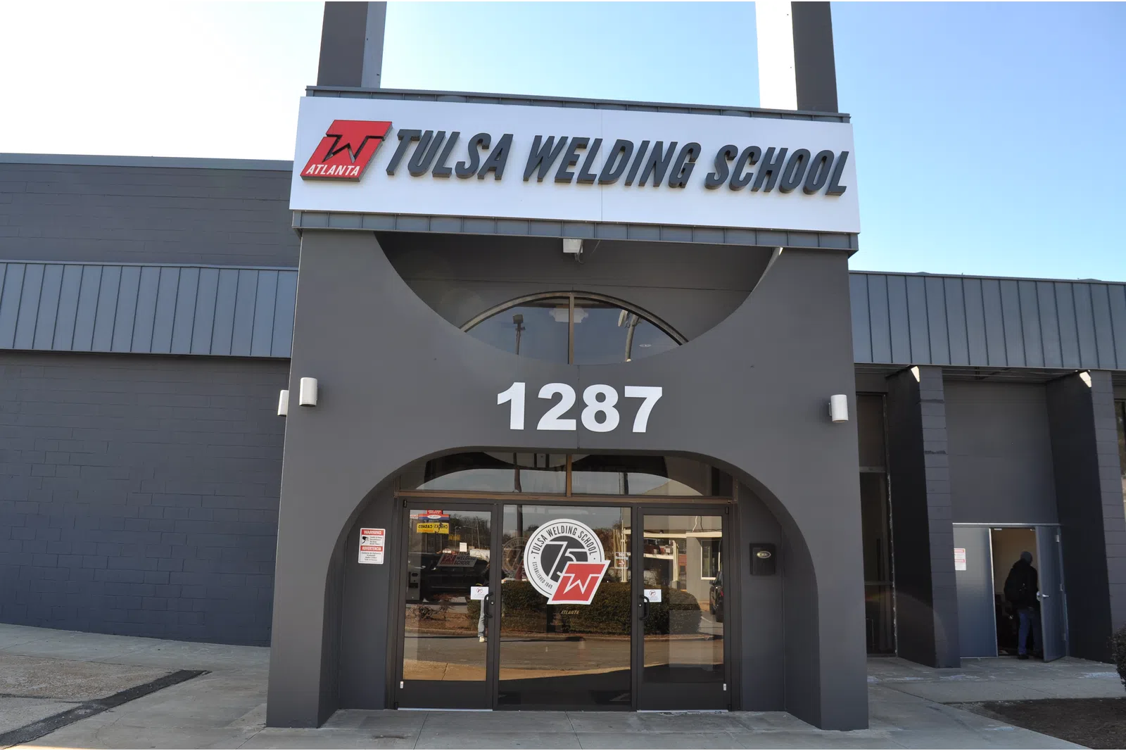 Entrance of Tulsa Welding School building with address 1287 and school logo on glass doors under clear sky.