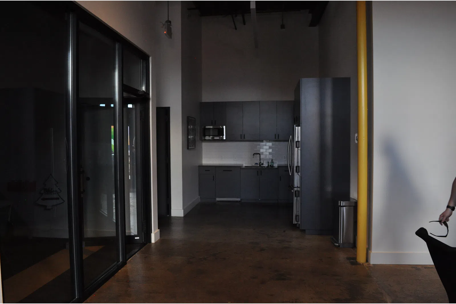 Modern office kitchenette with dark cabinets, stainless steel appliances, and polished concrete floor in open space.