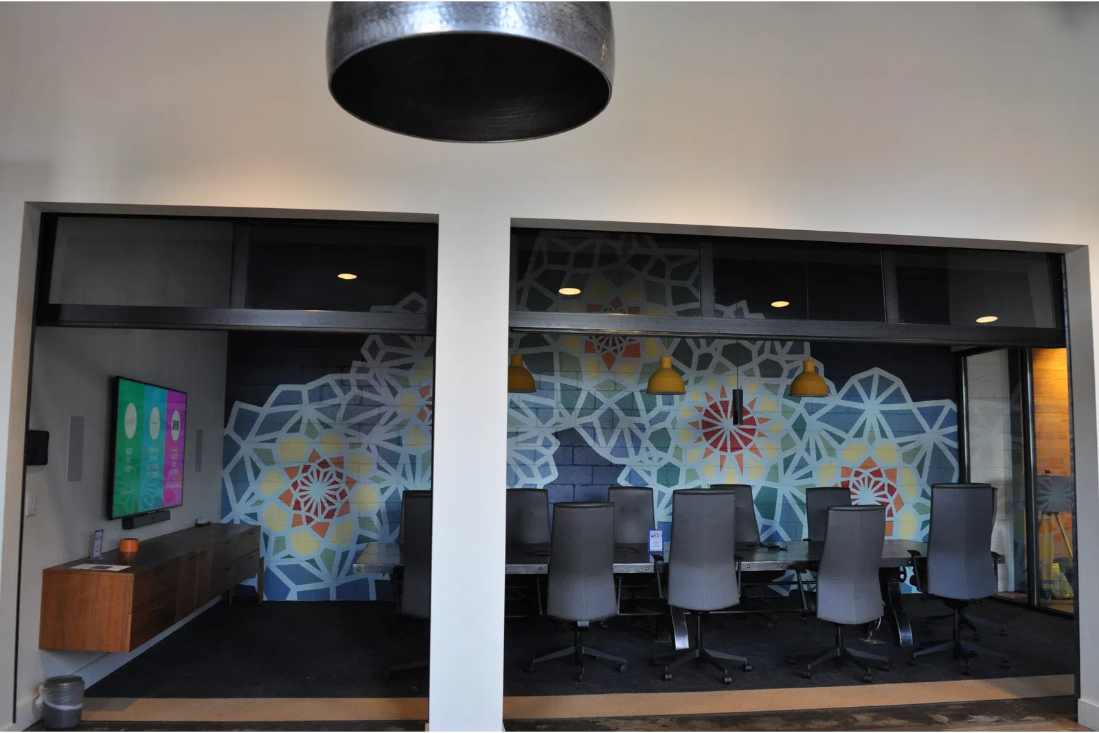 Modern conference room with colorful geometric wall art, black chairs, wooden table, and hanging pendant lights.