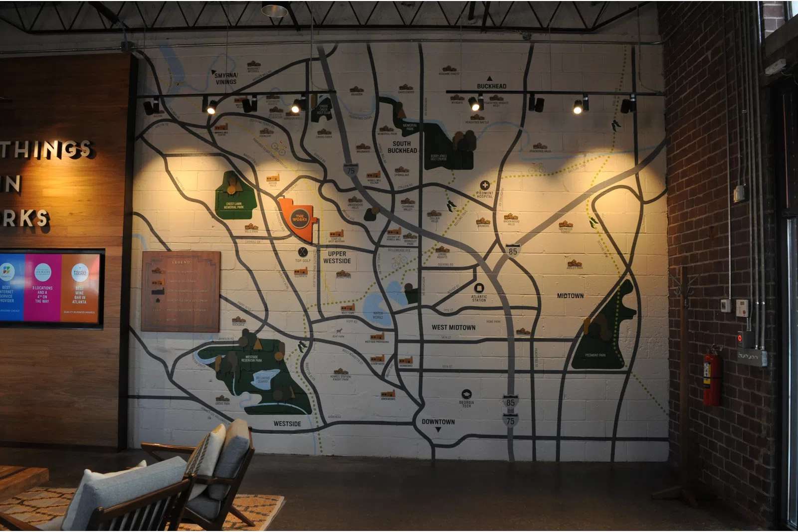 Large wall map of city neighborhoods and parks displayed in a modern indoor space with chairs and wooden decor.