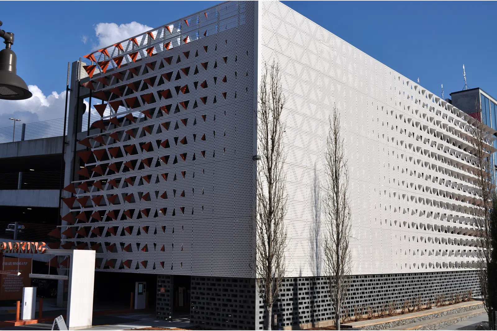 Modern parking garage with perforated metal facade featuring triangular patterns under a clear blue sky.