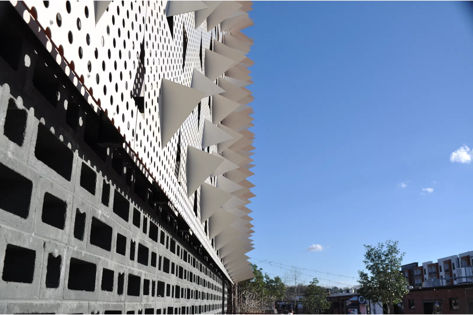 Modern building facade with geometric patterns and protruding white triangular shapes under a clear blue sky.