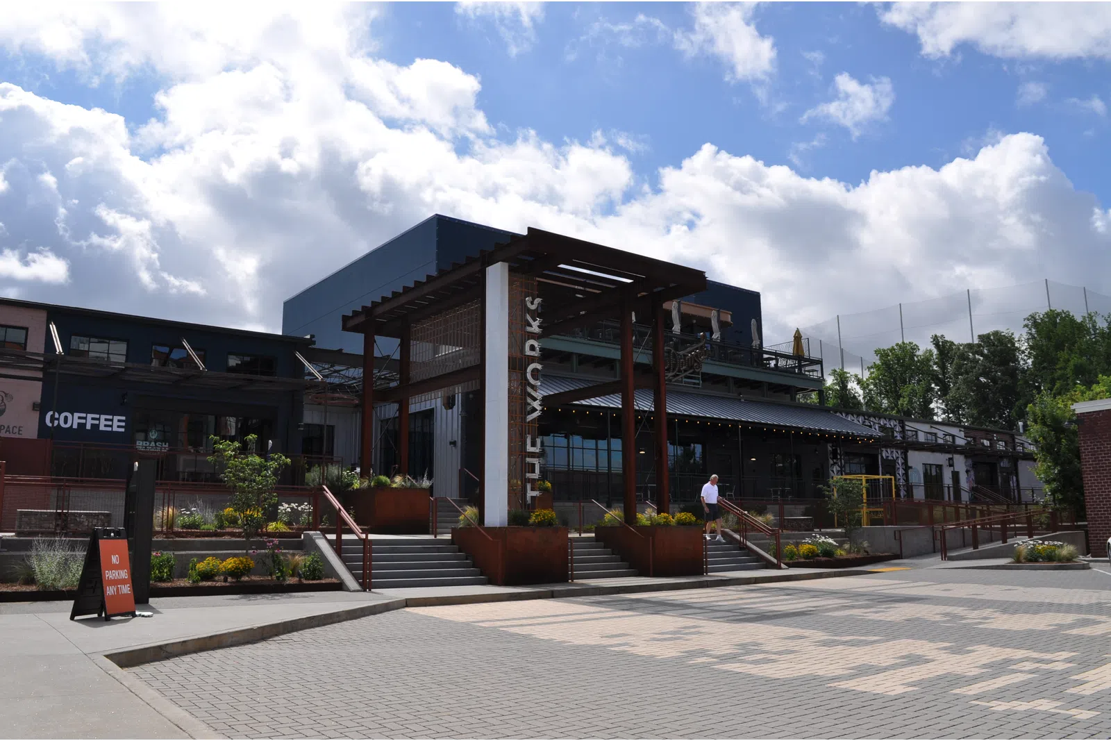 Modern commercial building with outdoor seating, coffee shop, and clear skies with scattered clouds.