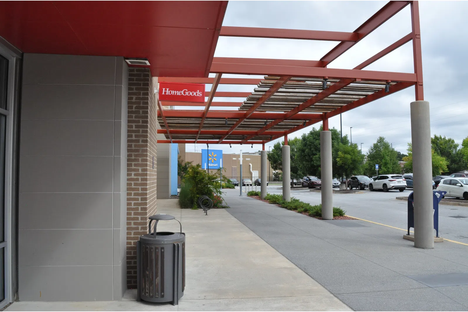 Outdoor shopping plaza with HomeGoods and Walmart stores under red metal canopy and parking lot on a cloudy day