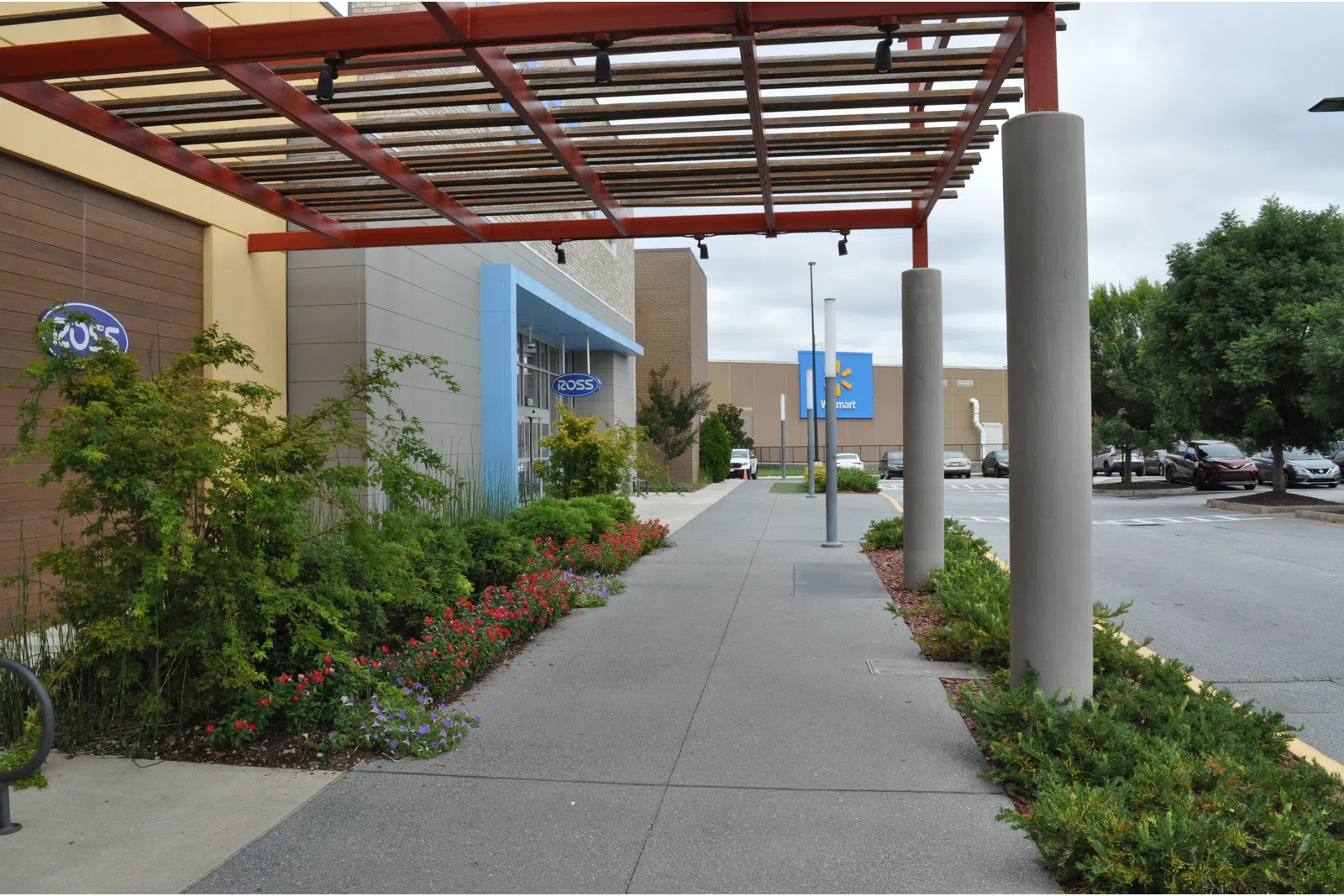 Outdoor shopping center walkway with Ross and Walmart stores, greenery, and covered pergola on a cloudy day.