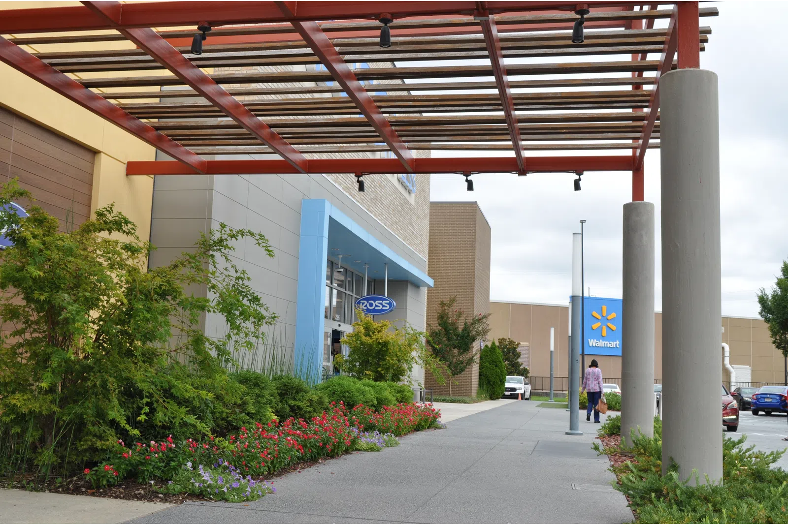 Outdoor walkway with modern pergola, landscaping, and store signs for Ross and Walmart on a cloudy day.