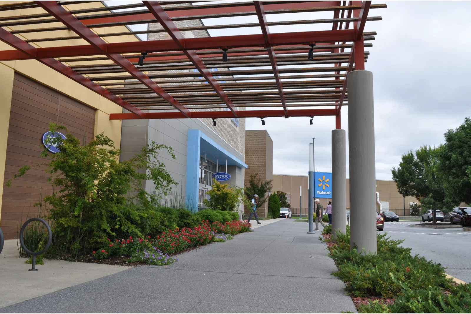 Outdoor walkway with a pergola, landscaped plants, and storefronts for Ross and Walmart in a shopping center.