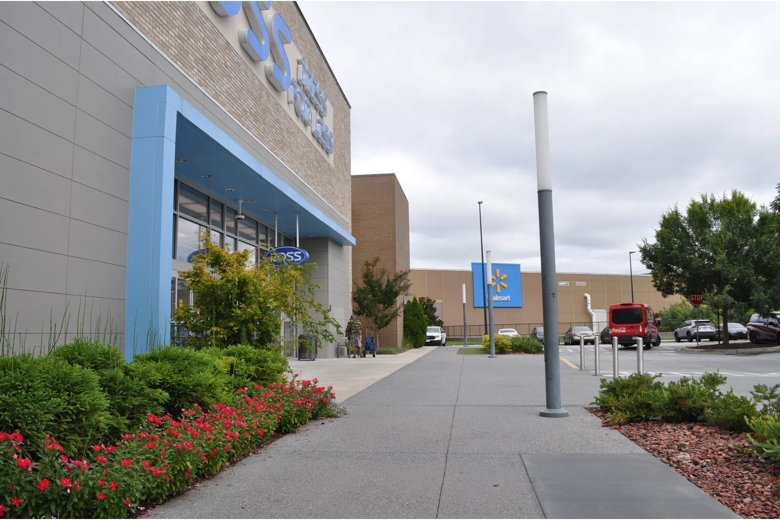 Outdoor view of a Ross Dress for Less store entrance with landscaping and a Walmart in the background under cloudy sky