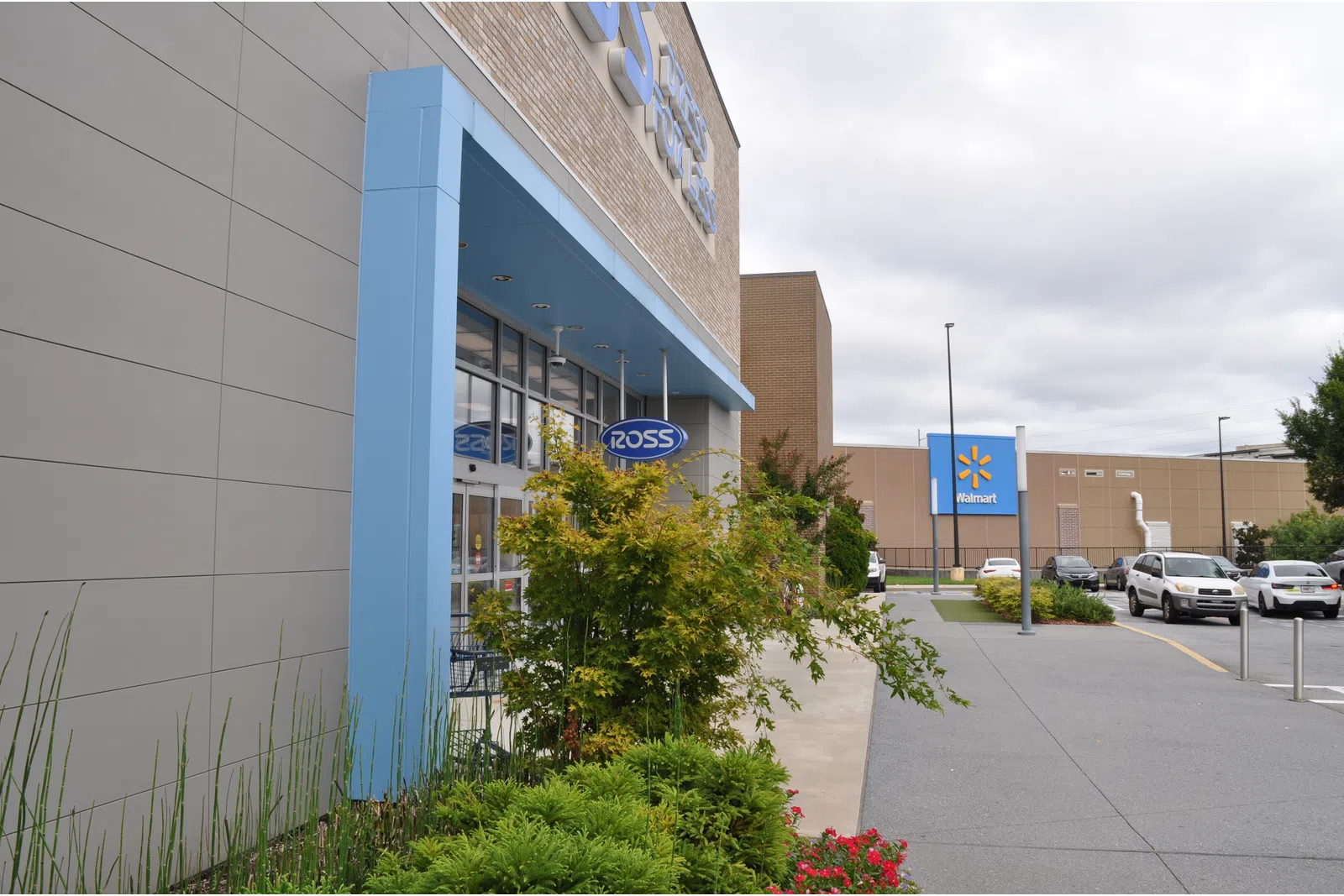 Exterior view of Ross store entrance with blue framing and Walmart building in the background under cloudy sky.