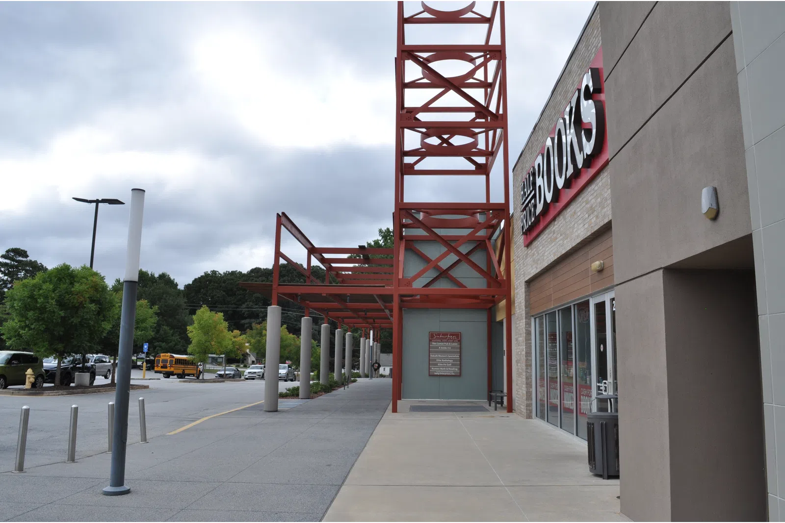Exterior view of a bookstore entrance with red metal framework and a cloudy sky overhead.