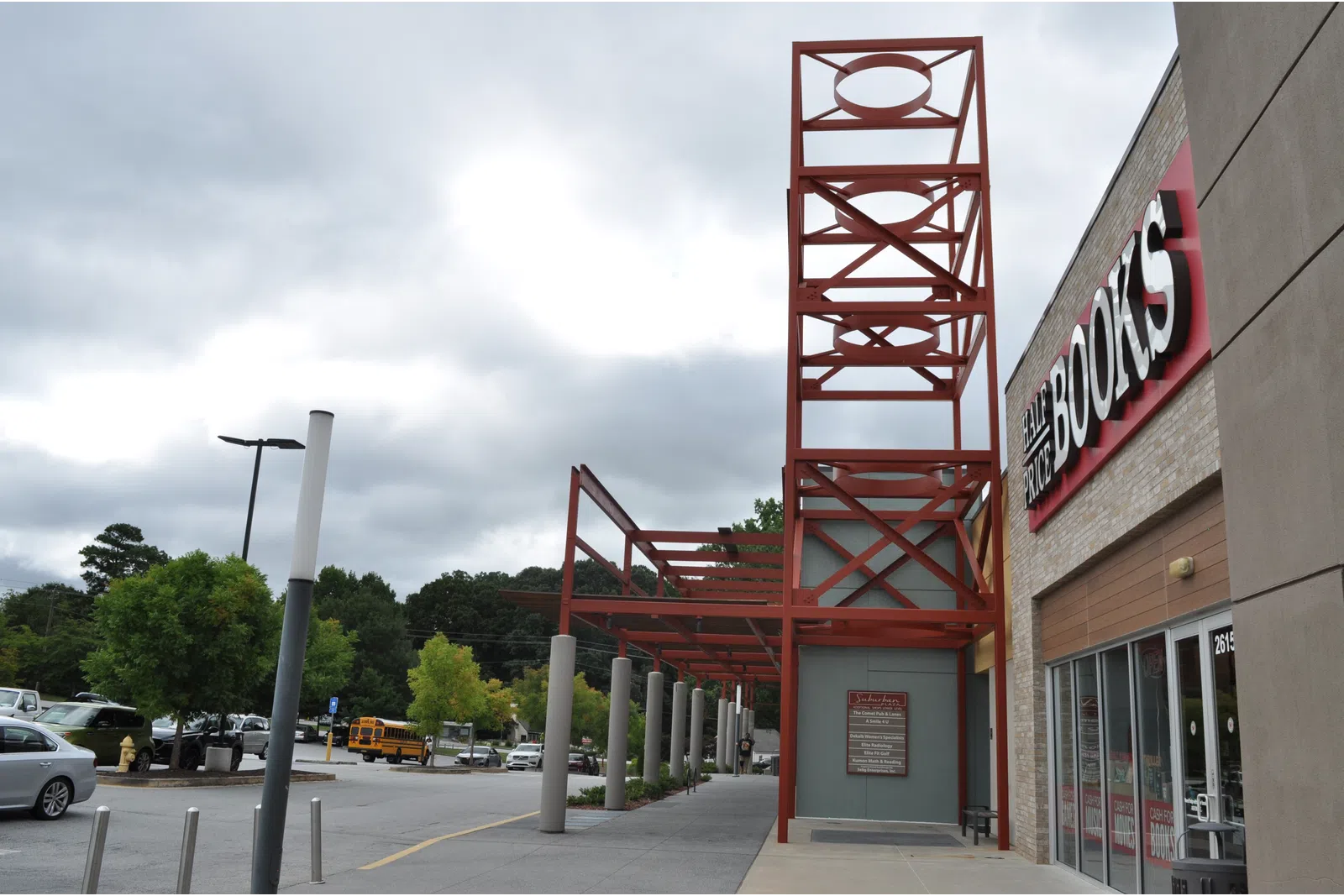 Exterior view of a bookstore with red metal framework and cloudy sky above a parking lot.