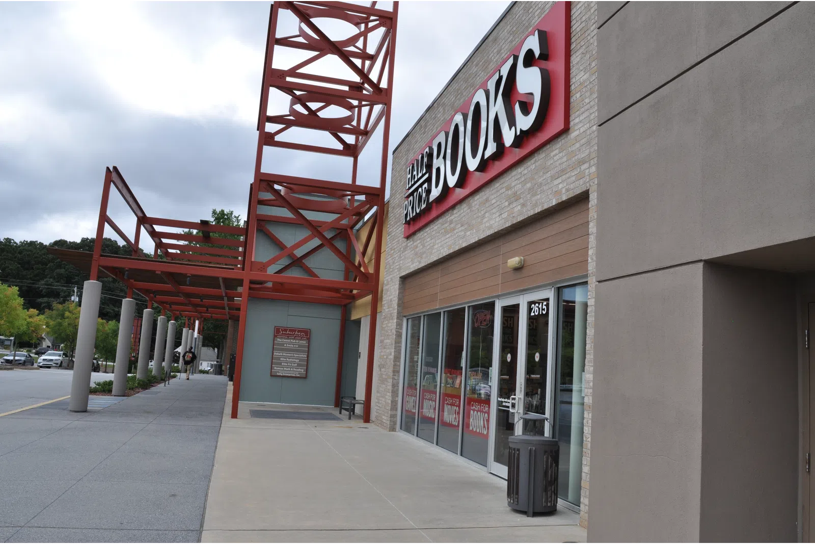 Exterior view of Half Price Books store with red metal framework and clear sidewalk under cloudy sky.