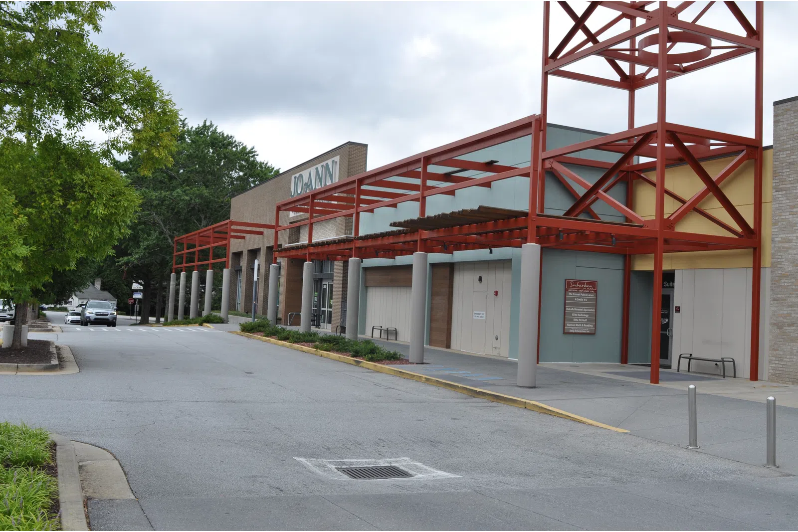 Exterior view of a Joann fabric and craft store with red metal awnings and a tree-lined parking area.