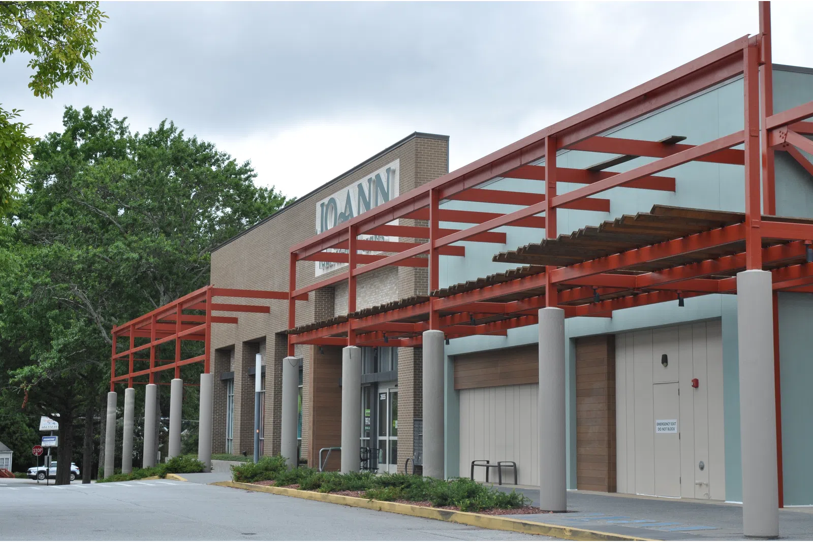 Exterior view of a Joann fabric and craft store with red metal framework and surrounding greenery