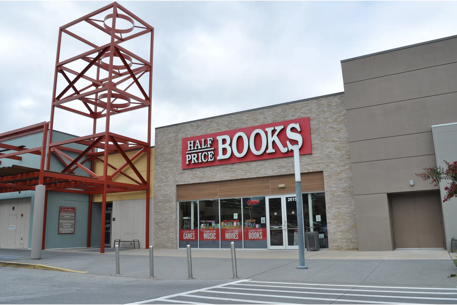 Half Price Books store exterior with large red and white sign and metal architectural feature against a cloudy sky.