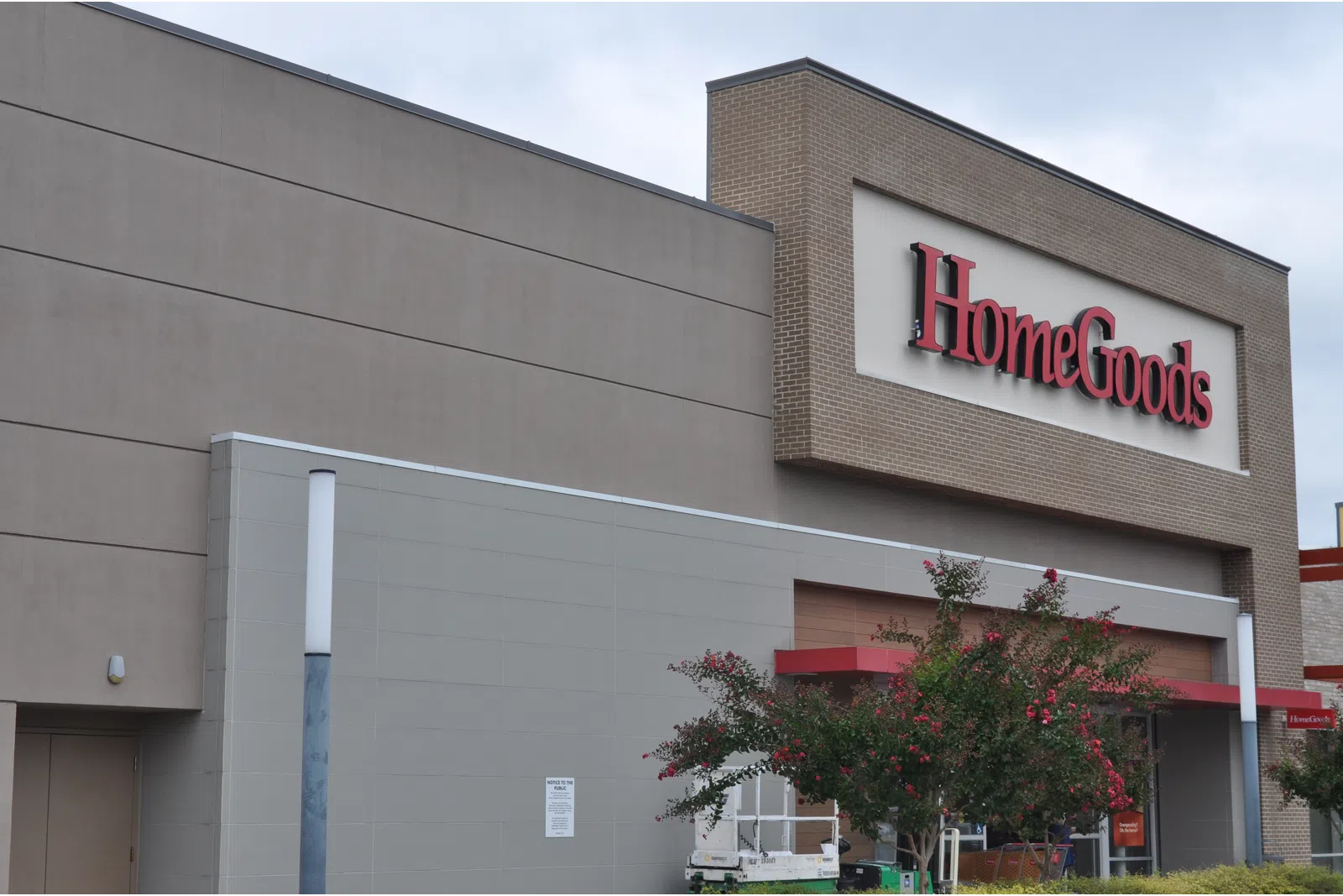 Exterior view of HomeGoods store with large red sign and landscaping including flowering trees.