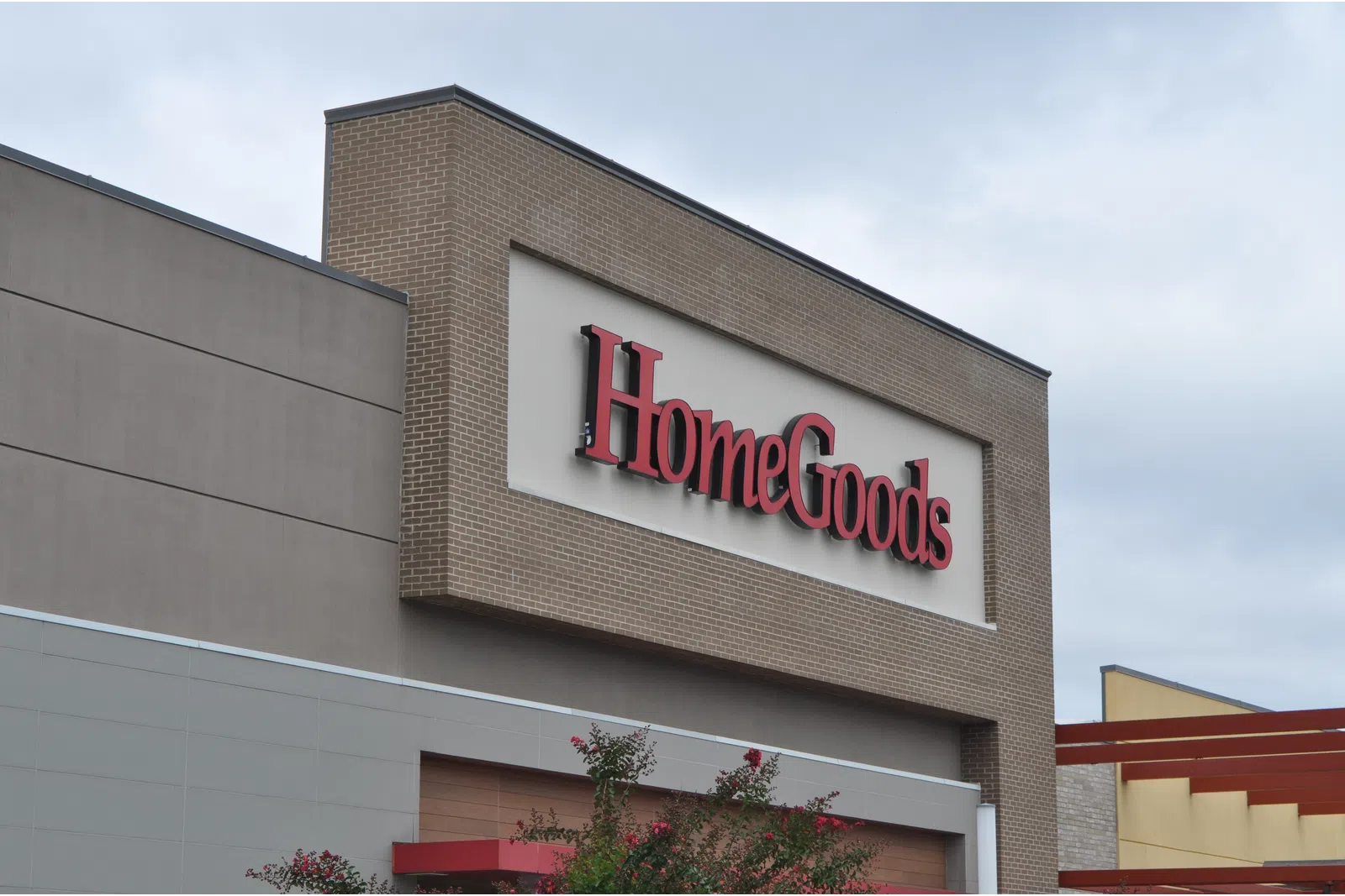 Exterior view of a HomeGoods store sign on a brick and beige building under a cloudy sky.