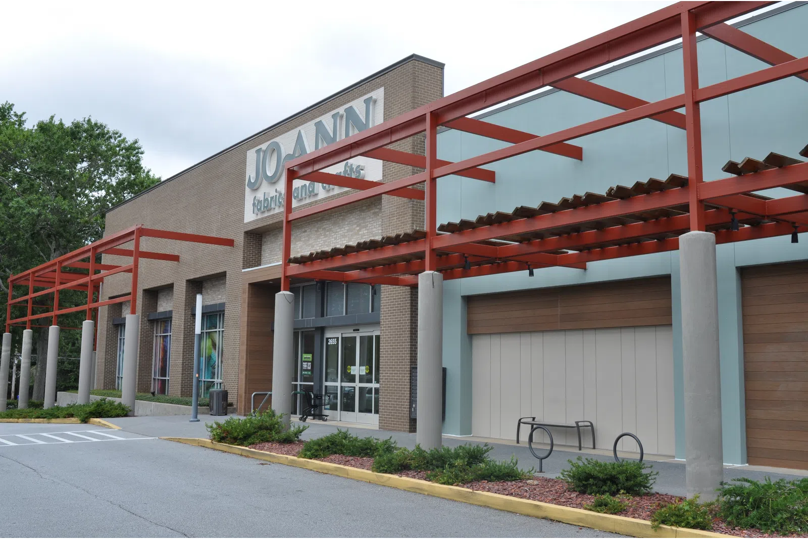 Exterior of a Joann Fabrics and Crafts store with red metal framework and glass windows on a cloudy day