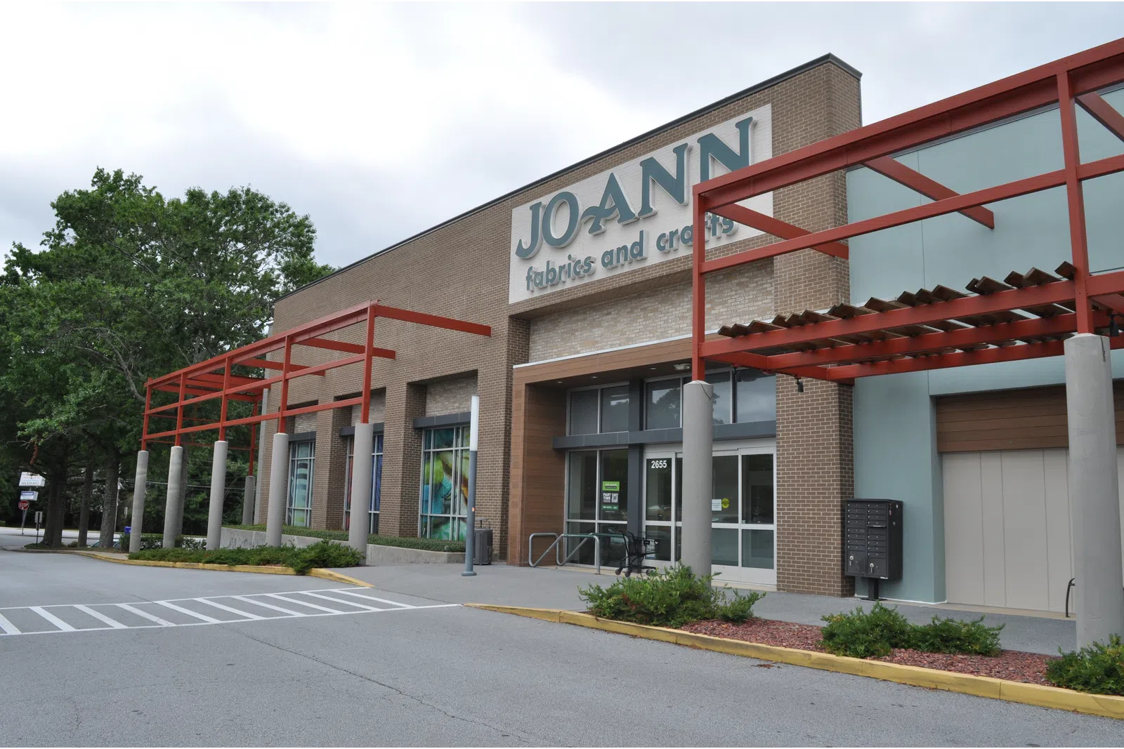 Exterior view of JOANN fabrics and crafts store with brick facade and red pergola on a cloudy day