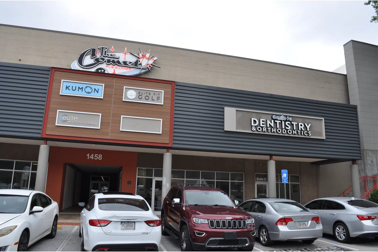 Exterior of a commercial building with signs for Kumon, Elite Golf, dentistry, and parked cars outside