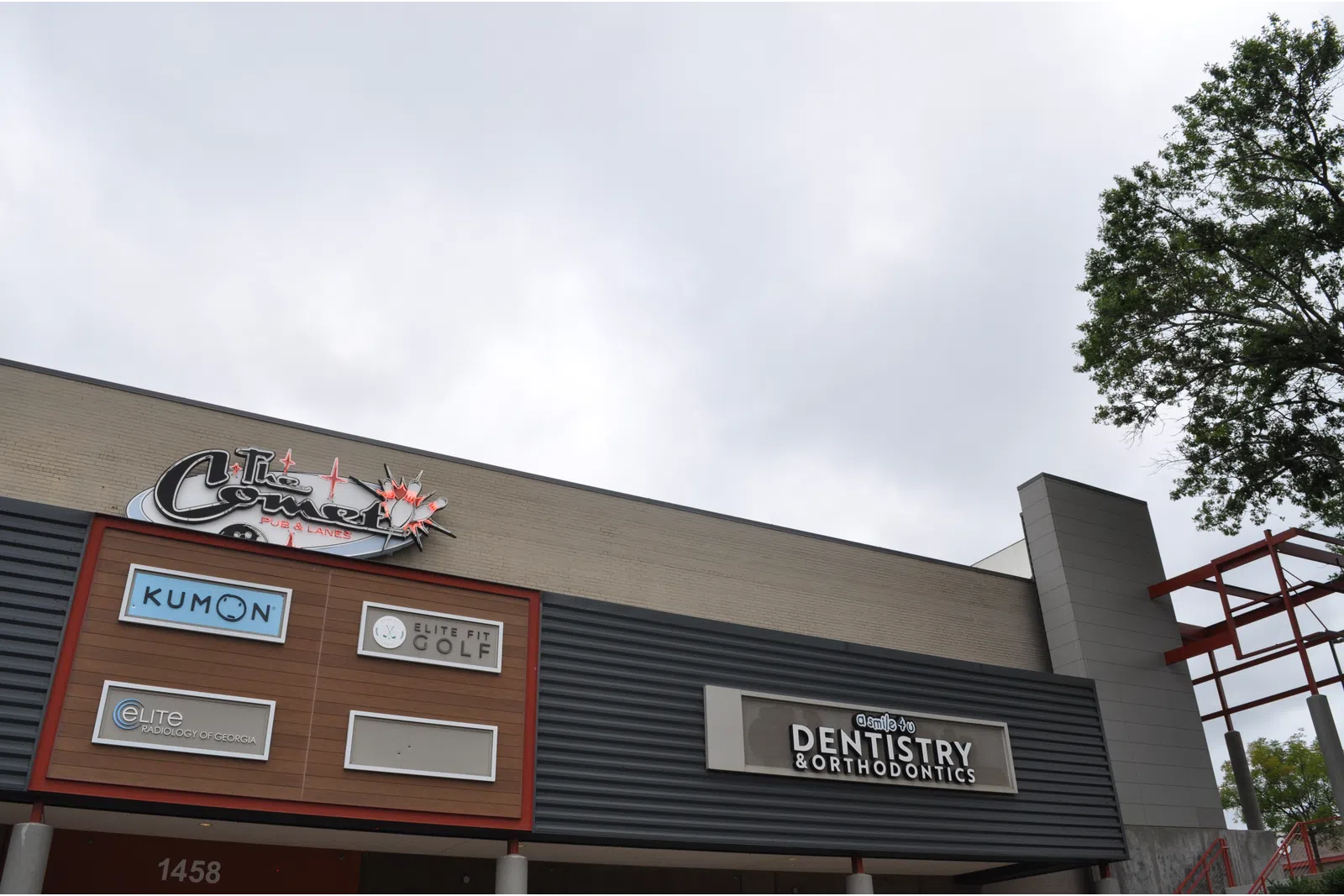 Commercial building facade featuring signs for Kumon, Elite Fit Golf, dentistry, and other businesses under a cloudy sky.