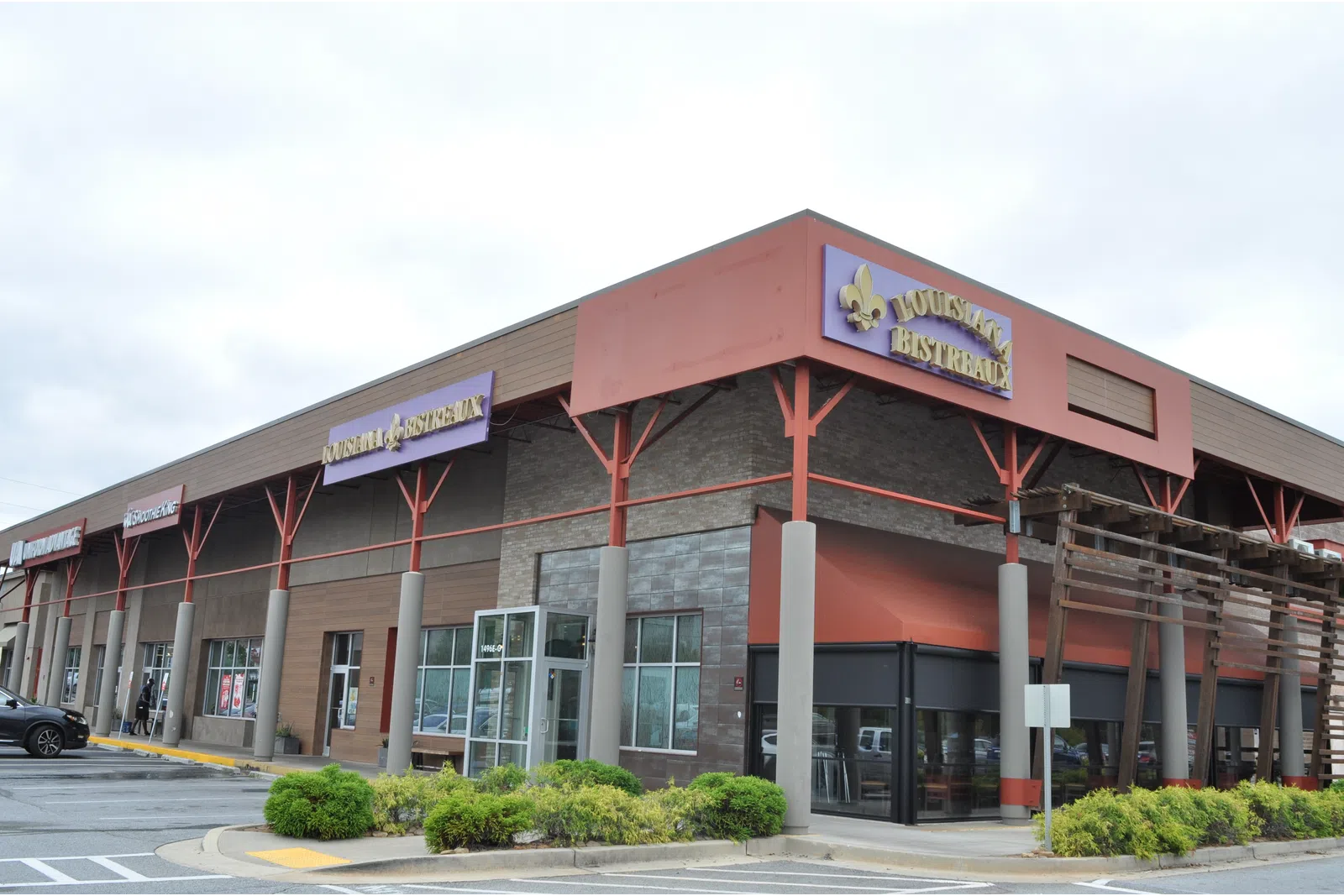Corner view of a shopping plaza with Louisiana Bistreaux restaurant and various stores under a cloudy sky.