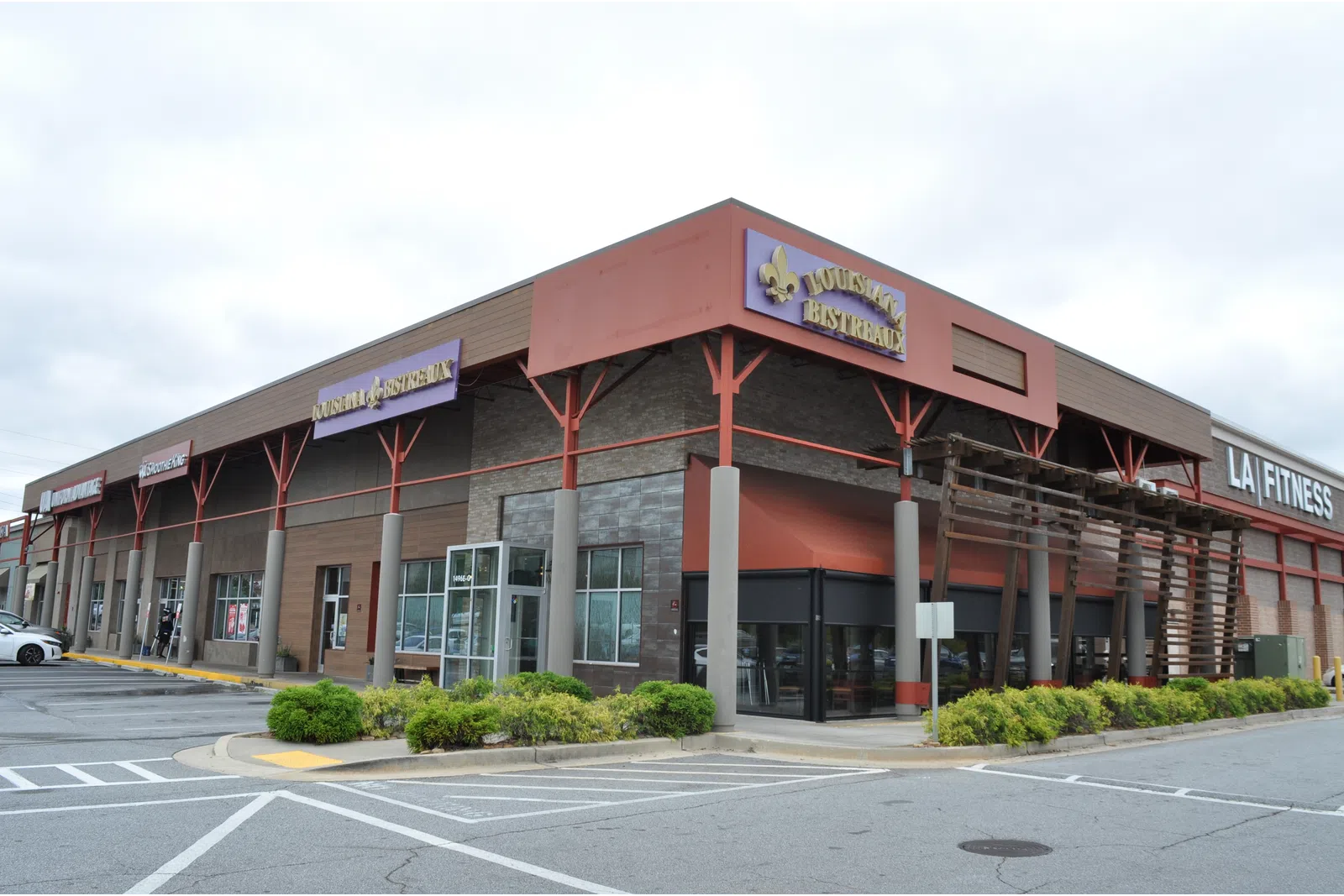 Exterior view of a shopping plaza featuring LA Fitness and Louisiana Bistreaux restaurants on a cloudy day.