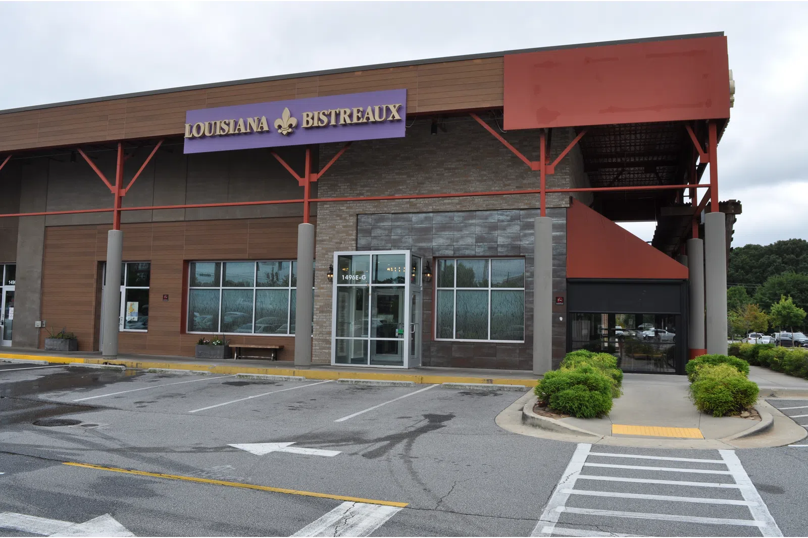 Front view of Louisiana Bistreaux restaurant with empty parking lot and greenery under cloudy sky.