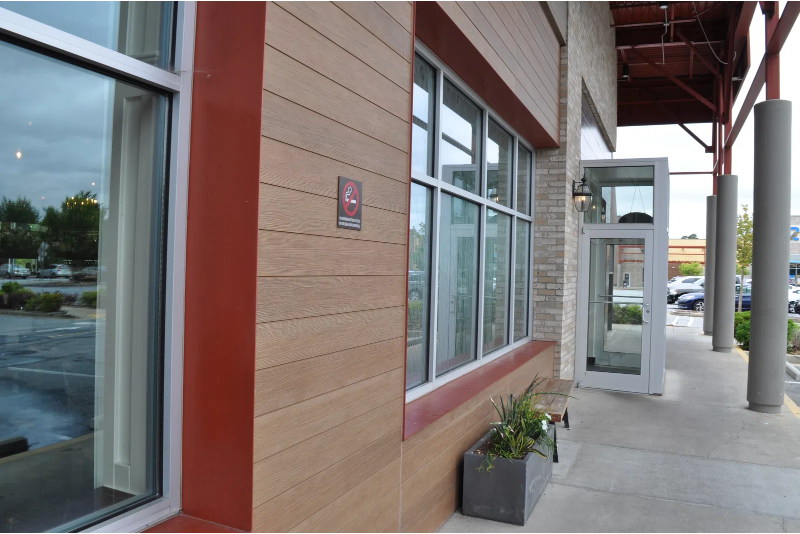 Modern building exterior with large windows, planter box, and an entry door under a covered walkway.