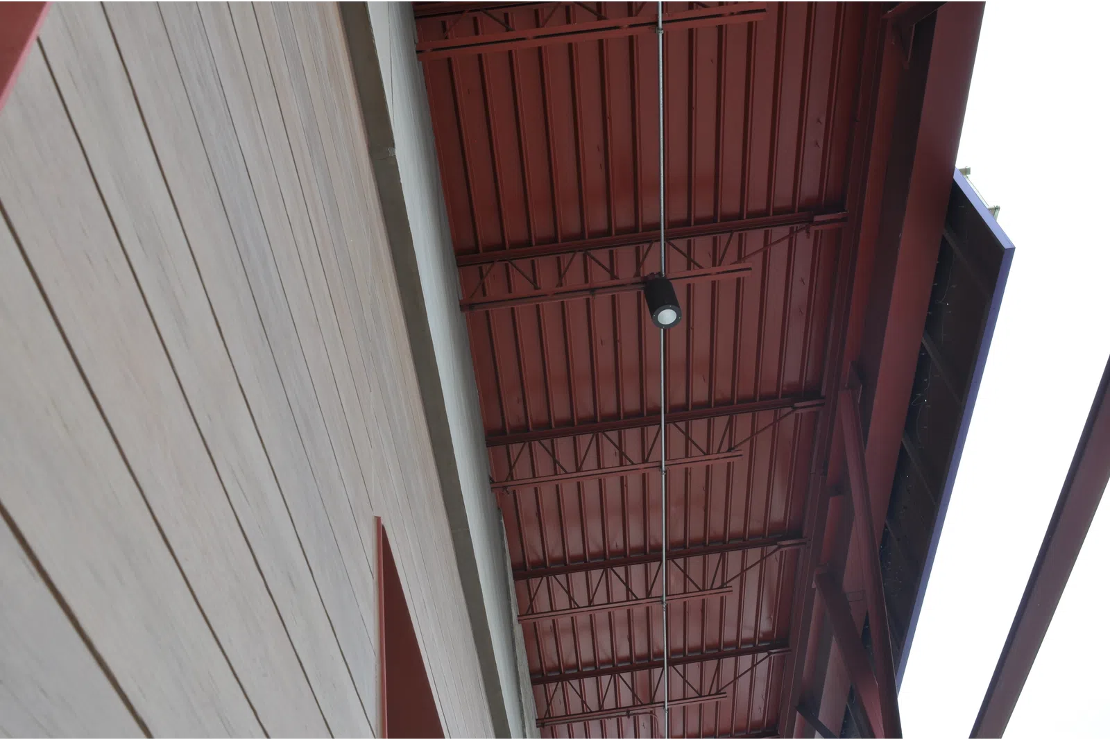 View looking up at a modern building's red metal ceiling and adjacent light-colored wood panel wall with a ceiling light fixture.