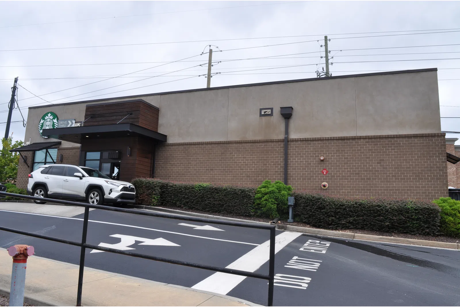 Exterior view of a Starbucks coffee shop with a white SUV parked and directional arrows on the road.