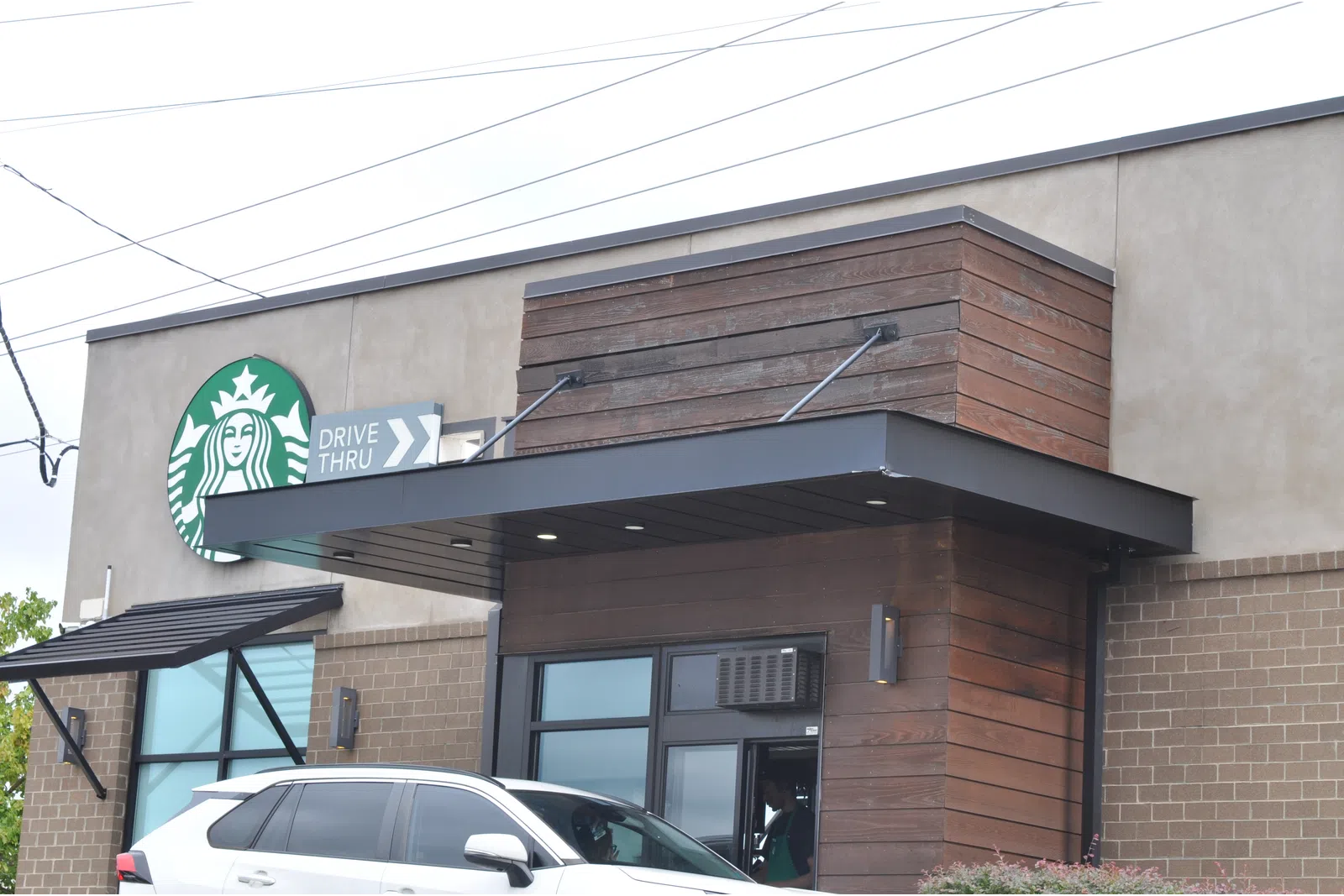 Starbucks coffee shop exterior with drive-thru lane and a white SUV parked nearby during daytime.