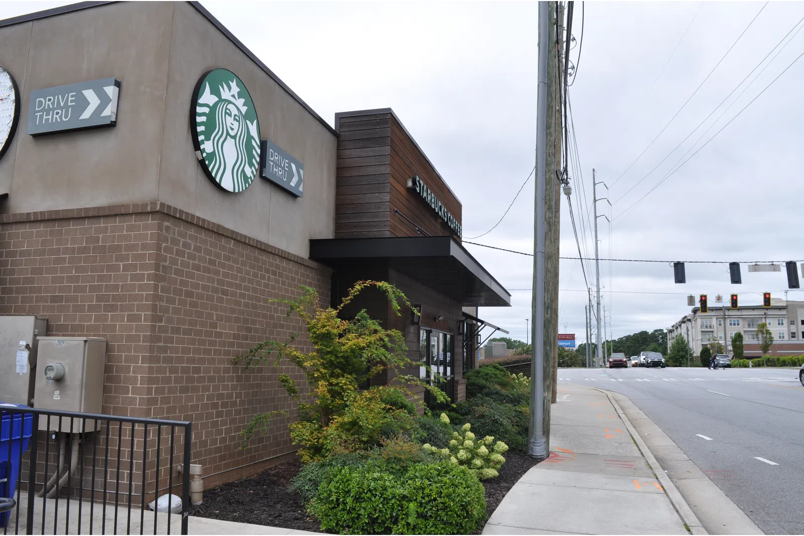 Exterior view of a Starbucks coffee shop with drive-thru signs and a nearby street intersection on a cloudy day