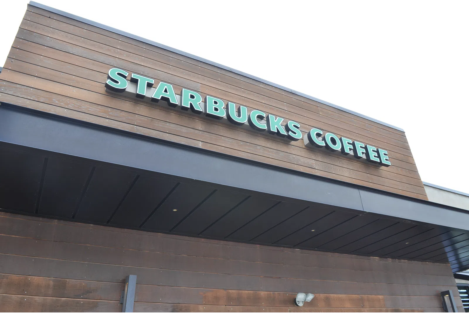 Exterior view of a Starbucks Coffee shop with wooden paneling and green signage on a clear day