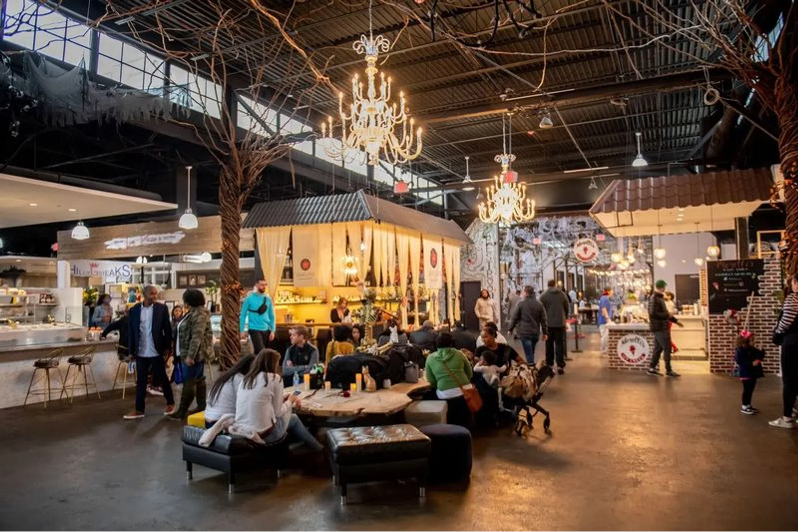 Indoor food market with people dining and walking under chandeliers and high ceiling lighting.