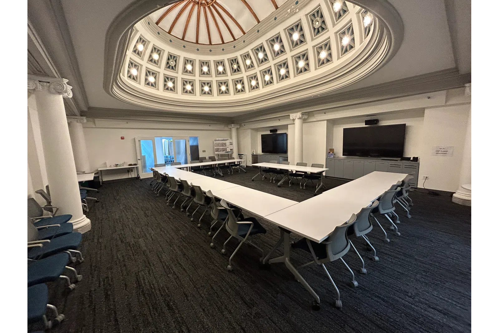 Conference room with U-shaped tables and chairs under a decorative domed ceiling with natural light.