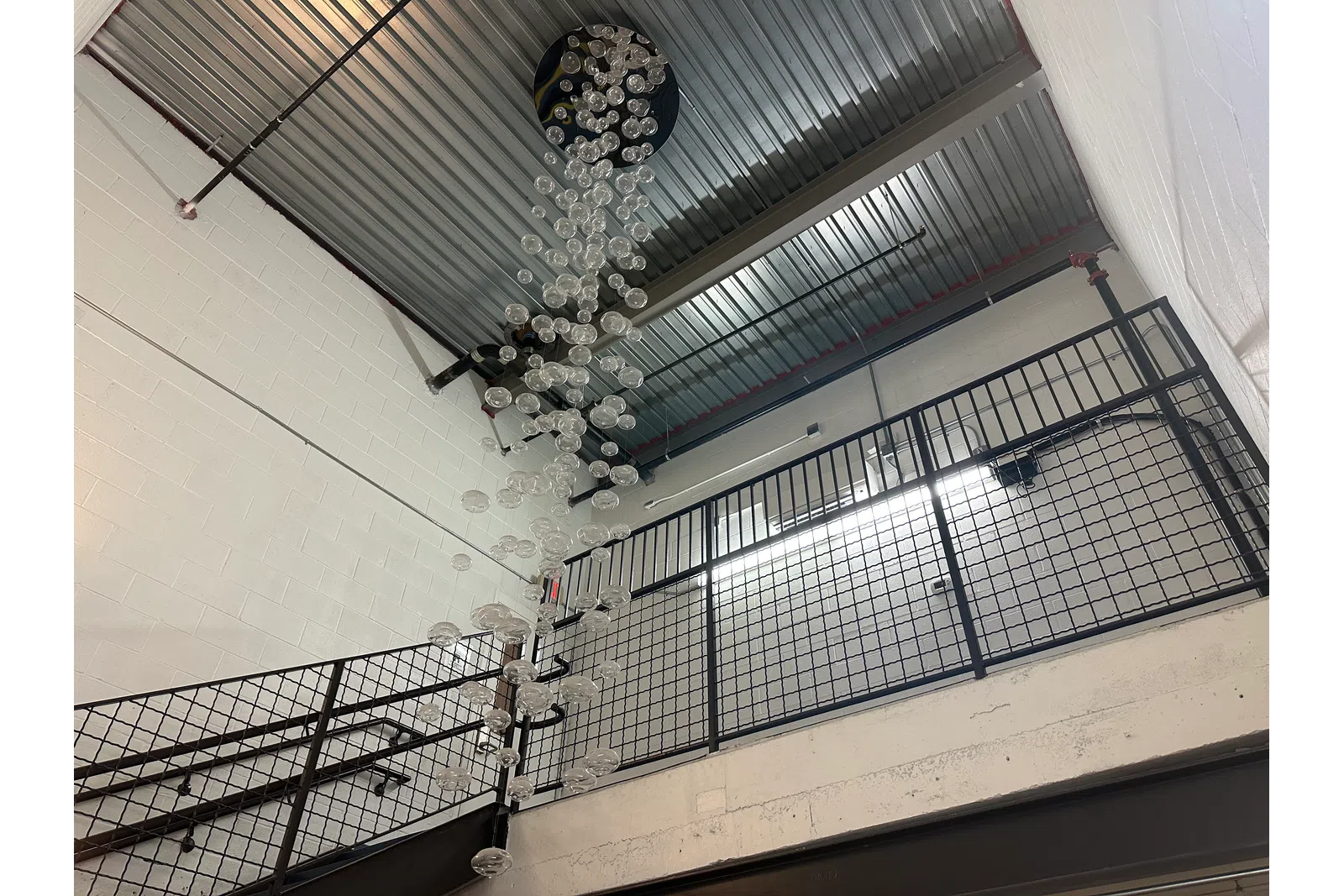 Modern indoor stairwell with metal railings and hanging glass bubble chandelier under industrial ceiling.