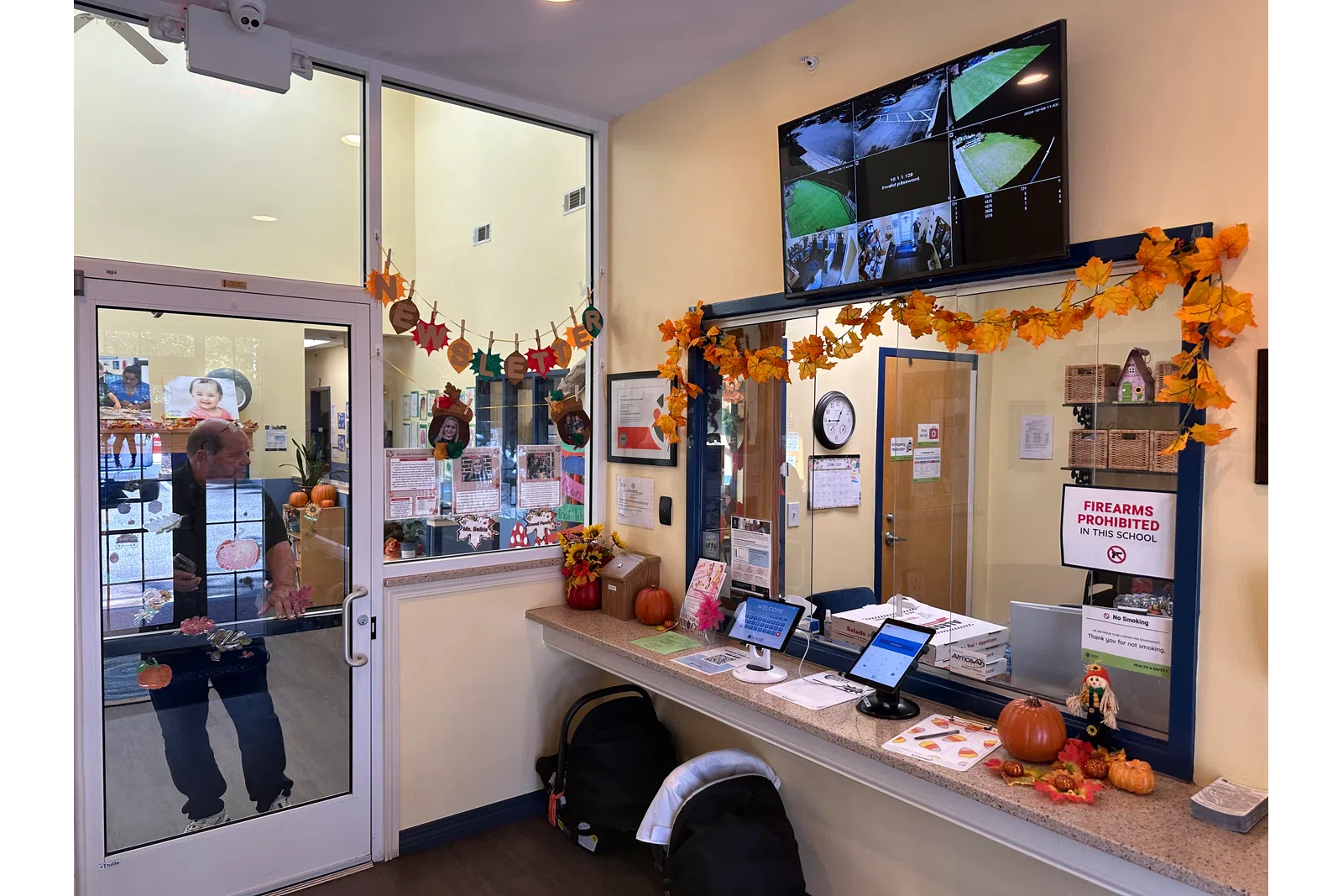 School office entrance decorated with autumn leaves, pumpkins, security monitors, and visitor check-in tablets.