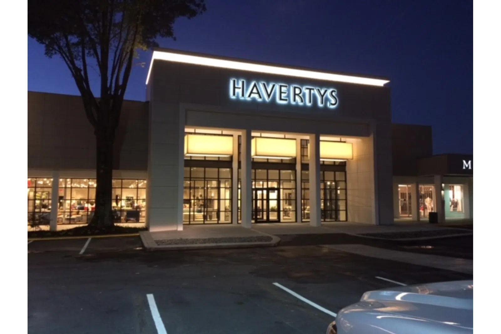 Havertys furniture store entrance illuminated at night with empty parking lot and tree in foreground