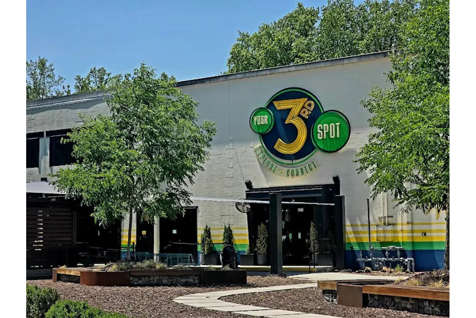 Exterior of a building with a large colorful 3rd Spot logo, surrounded by trees and outdoor seating area.