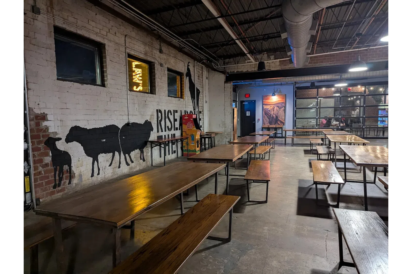 Interior of a rustic industrial dining area with wooden tables, benches, and animal murals on brick walls.