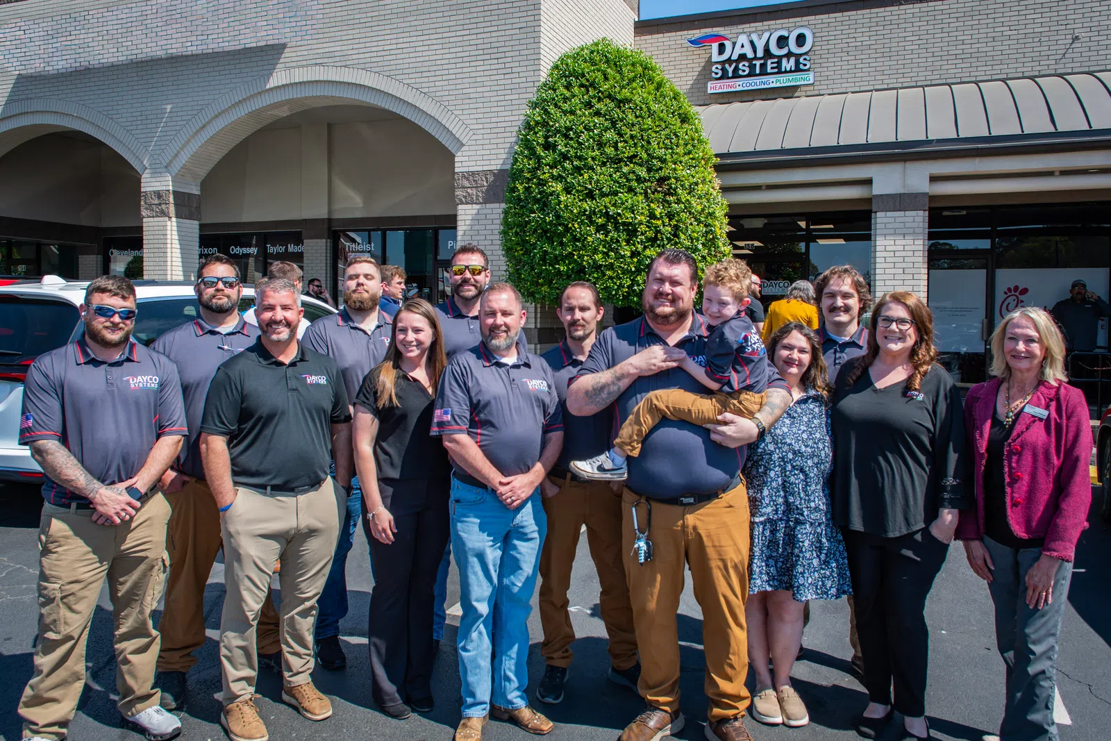 Group photo of Dayco Systems employees standing outside their office building on a sunny day.