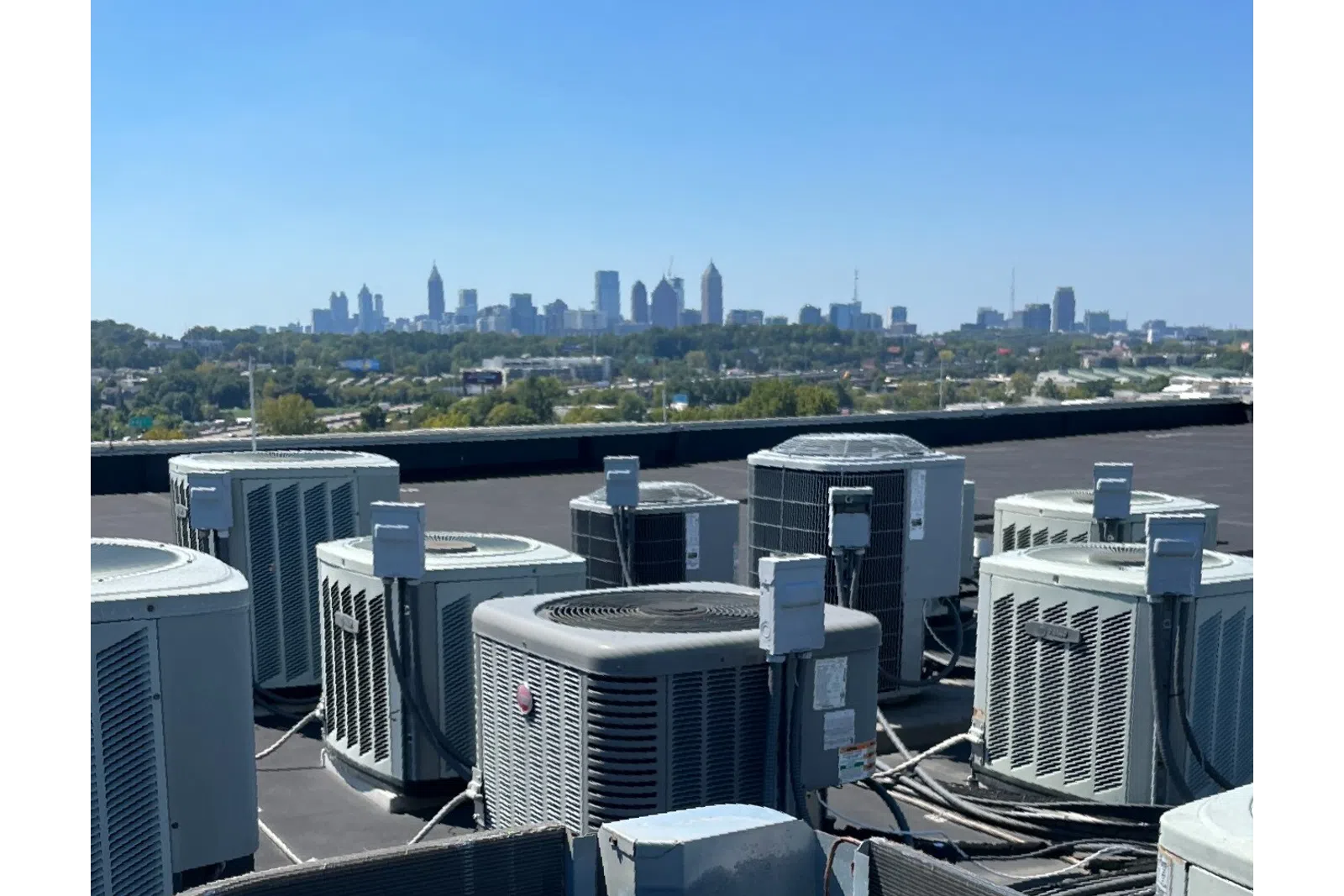 Multiple rooftop HVAC units installed on a building roof with the city skyline under clear blue sky