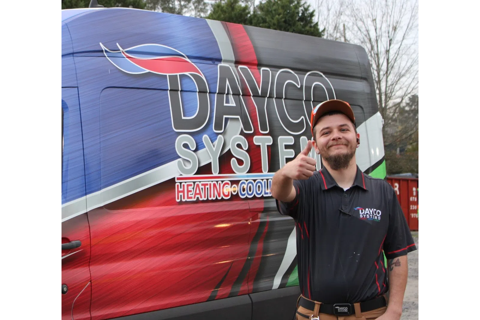 Smiling technician in Dayco Systems uniform gives thumbs up next to colorful Dayco Systems HVAC service van.