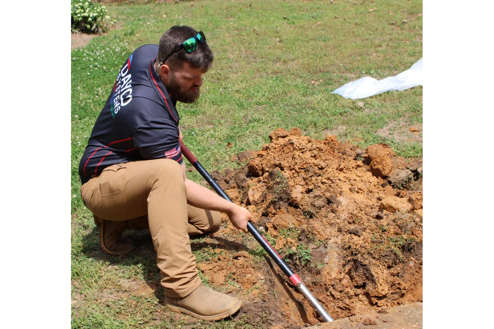 Man in work clothes digging a hole in the ground with a shovel on a grassy area to fix plumbing leak during daytime