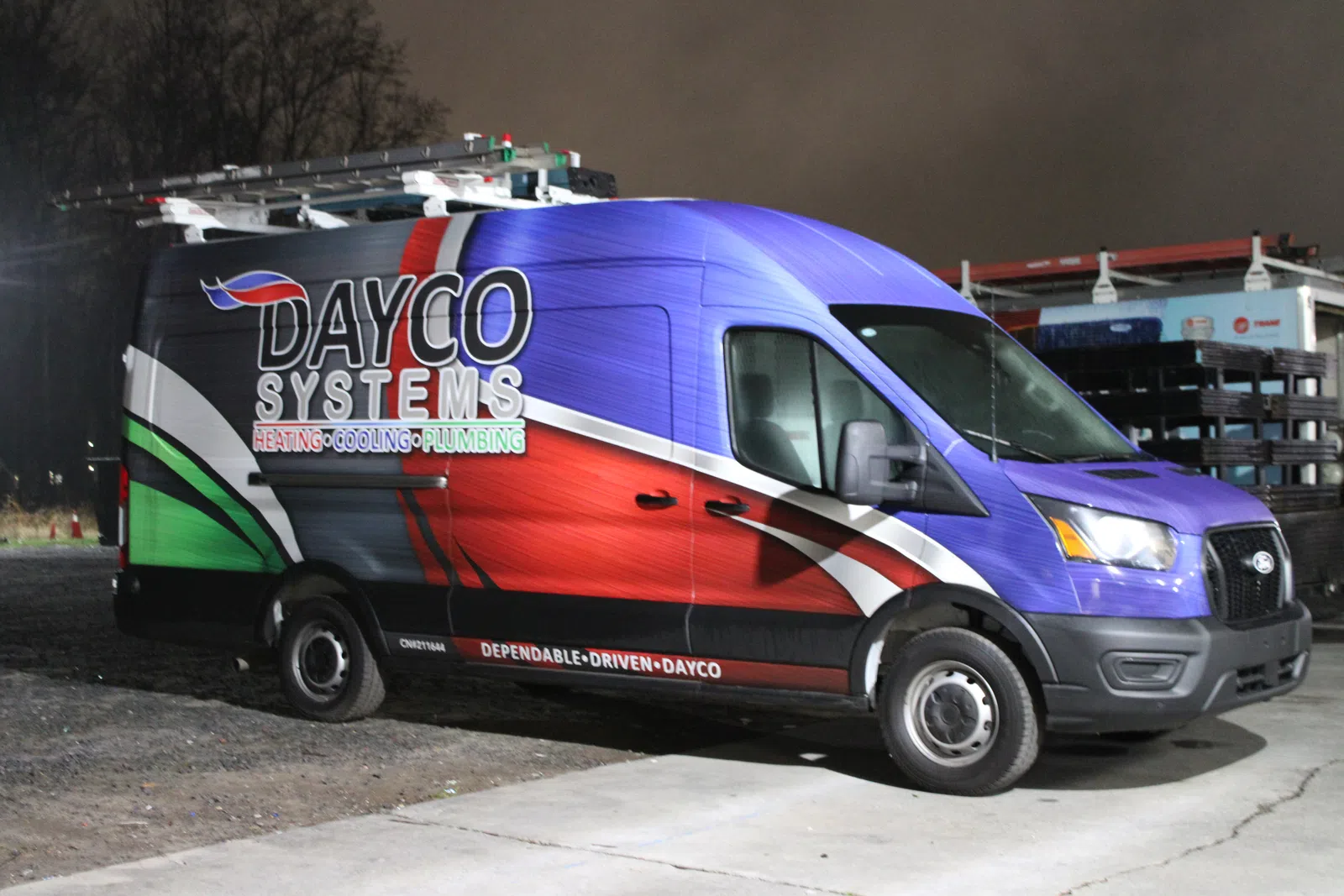 Dayco Systems heating, cooling, and plumbing service van with colorful branding parked outdoors at night.